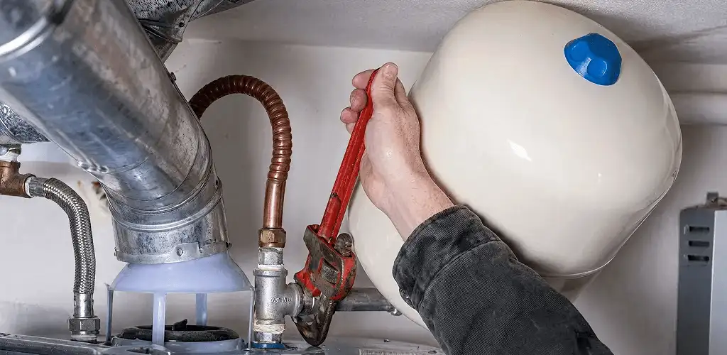 Water heater repair technician tightening plumbing connections near a tank unit in Duluth, MN